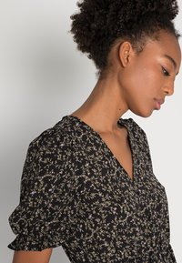 Vestido preto floral com mangas bufantes, apresentando um decote em V e um intricado padrão floral em tons de roxo e verde num tecido suave.