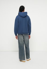 Mørkeblå hettegenser med avslappet passform, paret med lyse, vide jeans og hvite sneakers. Enkel tekstur og minimale detaljer.