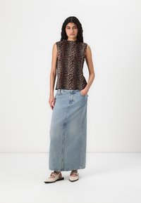 Top senza maniche con stampa animalier in marrone e nero, abbinato a una gonna maxi in denim blu chiaro, con orlo leggermente strappato e tasche.