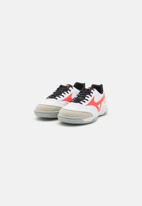 Zapatillas deportivas blancas con acentos en rojo y negro, parte superior de cuero texturizado y malla, cuello acolchado y suela de goma gris con patrón de tracción.