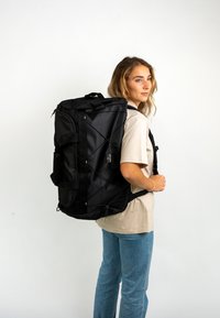 Black duffel-style backpack with adjustable straps, textured fabric, zippered compartments, and a front bungee cord detail for extra storage.