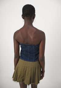 Denim strapless top with gathered seams, paired with an olive green pleated mini skirt featuring frayed edges. Takana näky.