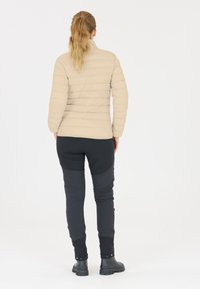 Lys beige dunjakke med høj krave, quiltet design og lange ærmer, parret med mørkegrå tapered bukser og sorte vandtætte støvler.