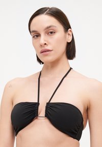 Svart stroppeløs bikinioverdel med rynket stoffdesign, tynne justerbare stropper og en sentral hardwaredetalj. Glatt, elastisk materiale.