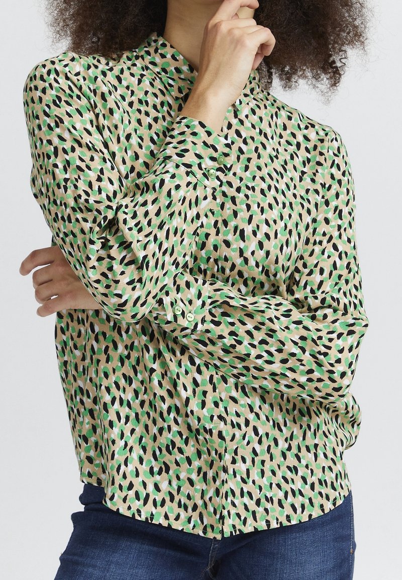 Blouse à manches longues en tissu léger avec imprimé léopard vert, crème et noir. Dotée d'un devant à boutons et d'un col.
