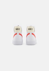 Bílé vysoké tenisky s červenými akcenty, z koženého a gumového materiálu, kulatá špička a značkové logo Nike na zadním podpatku.