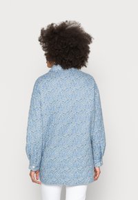 Button-up shirt in light blue fabric, featuring a white floral pattern, long sleeves, and a collared neckline, with a relaxed fit.