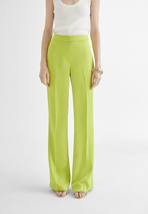 Pantaloni a gamba larga verde lime brillanti con vita alta, texture liscia e design plissettato, abbinati a una semplice canotta bianca.