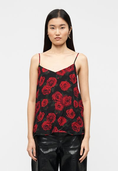 Camiseta negra con un estampado de rosas rojas, tirantes finos ajustables y un corte holgado. Combinada con pantalones negros brillantes y texturizados.