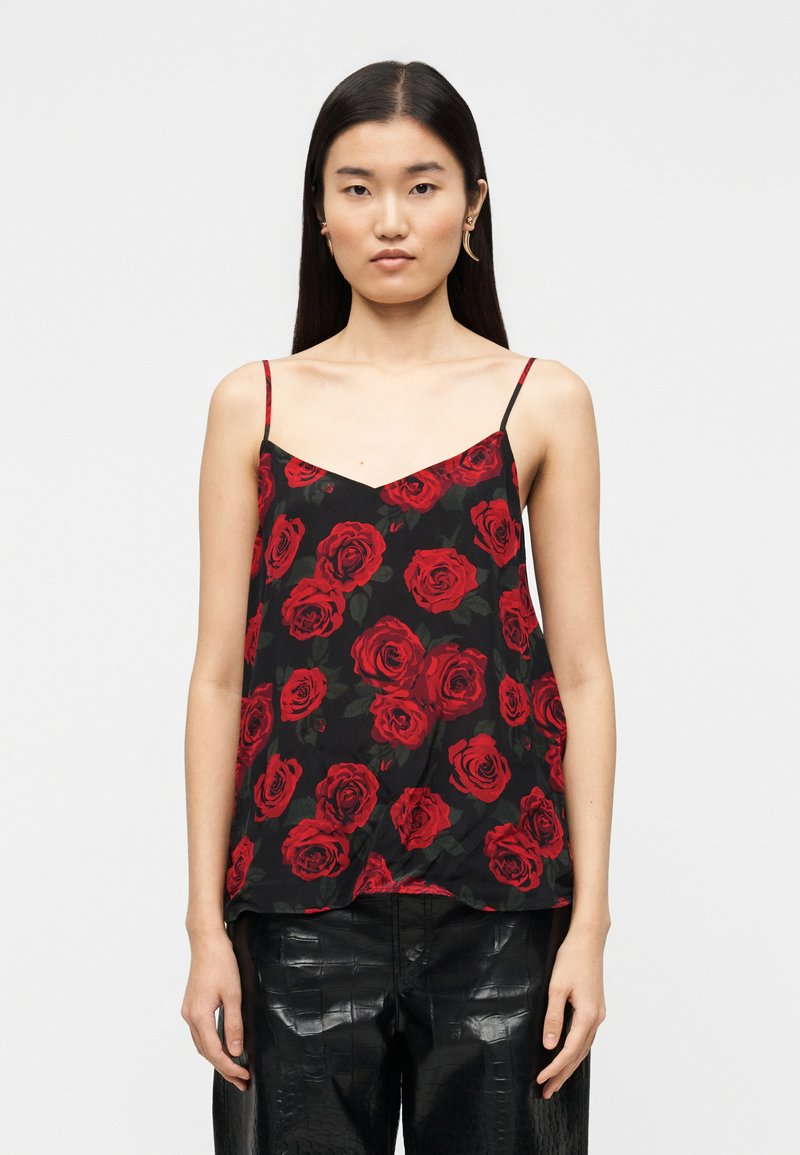 Μαύρο καμιζόλ με σχέδιο από κόκκινα τριαντάφυλλα, λεπτές ρυθμιζόμενες τιράντες και άνετη εφαρμογή. Φοριέται με λαμπερό μαύρο παντελόνι με υφή.