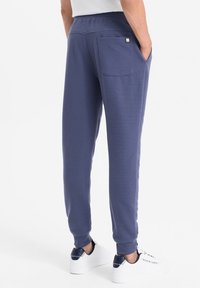 Námořnické tepláky s ribovanou texturou, elastickým pasem a zadními kapsami. V kombinaci s bílými teniskami s námořnickými akcenty.