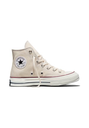 Baskets montantes beige Converse Chuck Taylor All Star avec semelle en caoutchouc blanche, logo étoile noir et lacets défaits sur fond blanc.