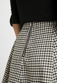 Gonna a scacchi bianco e nero in tessuto testurizzato, con zip laterale e silhouette svasata.