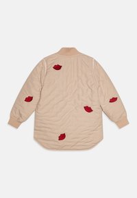 Beige quiltet jakke med ribbet krave og rød læbe-formet broderi på ryggen. Har lange ærmer og en let buet kant.