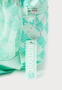 Sac à dos vert menthe clair en tissu maillé et solide, comportant une étiquette "Just Do It" et des accents en métal argenté. Surface texturée avec un motif design.