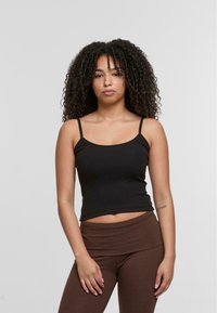 Black ribbed tank top with thin straps, fitted design, and a cropped length, paired with brown high-waisted leggings.