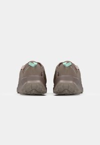 Baskets de trail running marron avec une semelle en caoutchouc texturée, un empiècement supérieur rembourré et une languette de talon vert menthe. Œillets renforcés pour un laçage sécurisé.