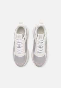 Zapatillas de cordones que presentan una mezcla de ante gris claro y beige y materiales sintéticos, con una lengüeta acolchada y cordones blancos.