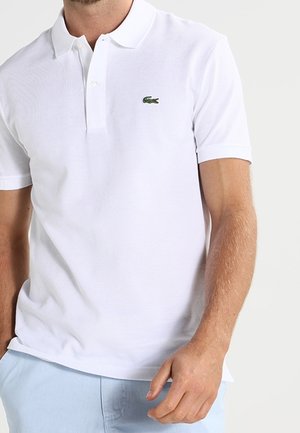 Polo blanca hecha de algodón texturizado con mangas cortas. Cuenta con una tapeta de tres botones y un pequeño logo de cocodrilo verde en el pecho.