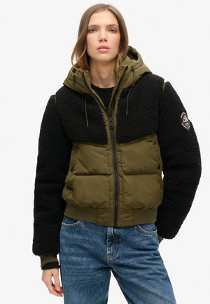 Dikke jas met een groene nylon body en zwarte fleece mouwen. Voorzien van een capuchon, ritssluiting en geribbelde manchetten. Geborduurd logo op de mouw.