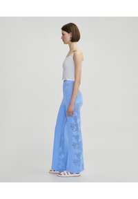Luchtige blauwe broek met een textuurpatroon, gecombineerd met een witte cropped tanktop en witte sandaaltjes met bandjes.