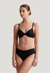 Zwart kant lingerie set met een beha met beugels en verstelbare bandjes, en bijpassende hooglopende slipjes met geometrische patronen.