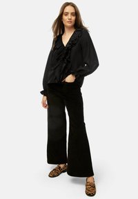 Black ruffled blouse with a deep V-neck, paired with high-waisted black corduroy flared pants and animal print slip-on shoes.