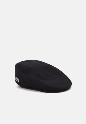 Czarna wełniana czapka typu flat cap z zaokrągloną koroną, z małym zielono-białym logo Lacoste z boku. Miękka tekstura i klasyczny design.