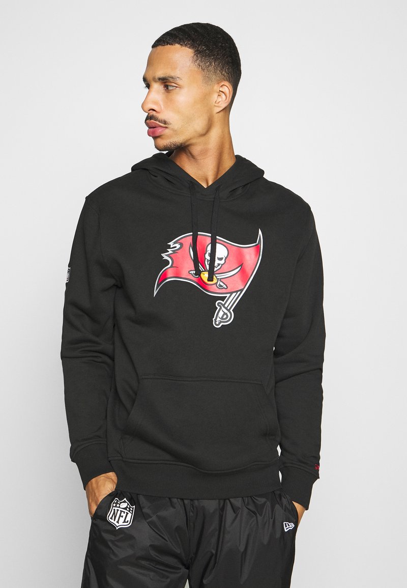 Haut à capuche noir avec un logo de drapeau des Buccaneers sur le devant, avec des cordons et une poche avant. Associé à un pantalon de sport noir.