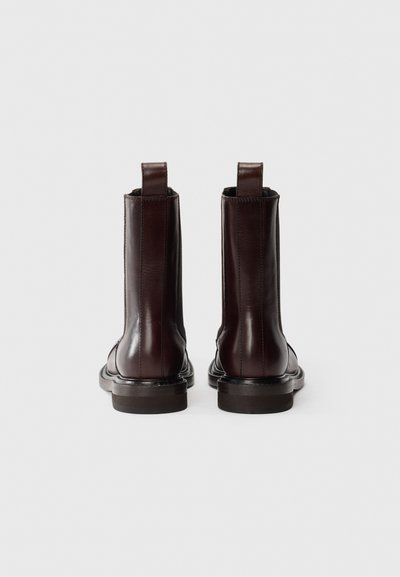 Stivaletti in pelle marrone con un design elegante, punte rotonde e piccoli passanti sul retro. Presentano dettagli cuciti e una suola resistente.