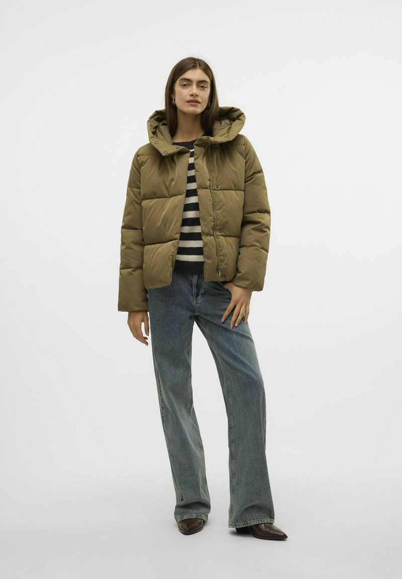 Giacca puffer color khaki con cappuccio, caratterizzata da un design trapuntato e chiusura frontale con zip. Abbinata a un top a righe e jeans a gamba larga.