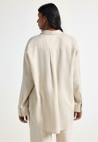 Beige linned skjorte med en afslappet pasform, lange ærmer og knapmanchetter. Har en rygslids og en klassisk krave. Glat tekstur.