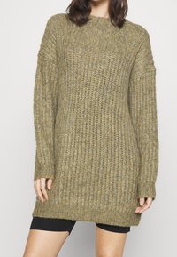 Gestrickter Pullover in Olivgrün, mit lockerer Passform, geripptem Texture, langen Ärmeln und rundem Halsausschnitt. Der Saum reicht bis über die Oberschenkel.