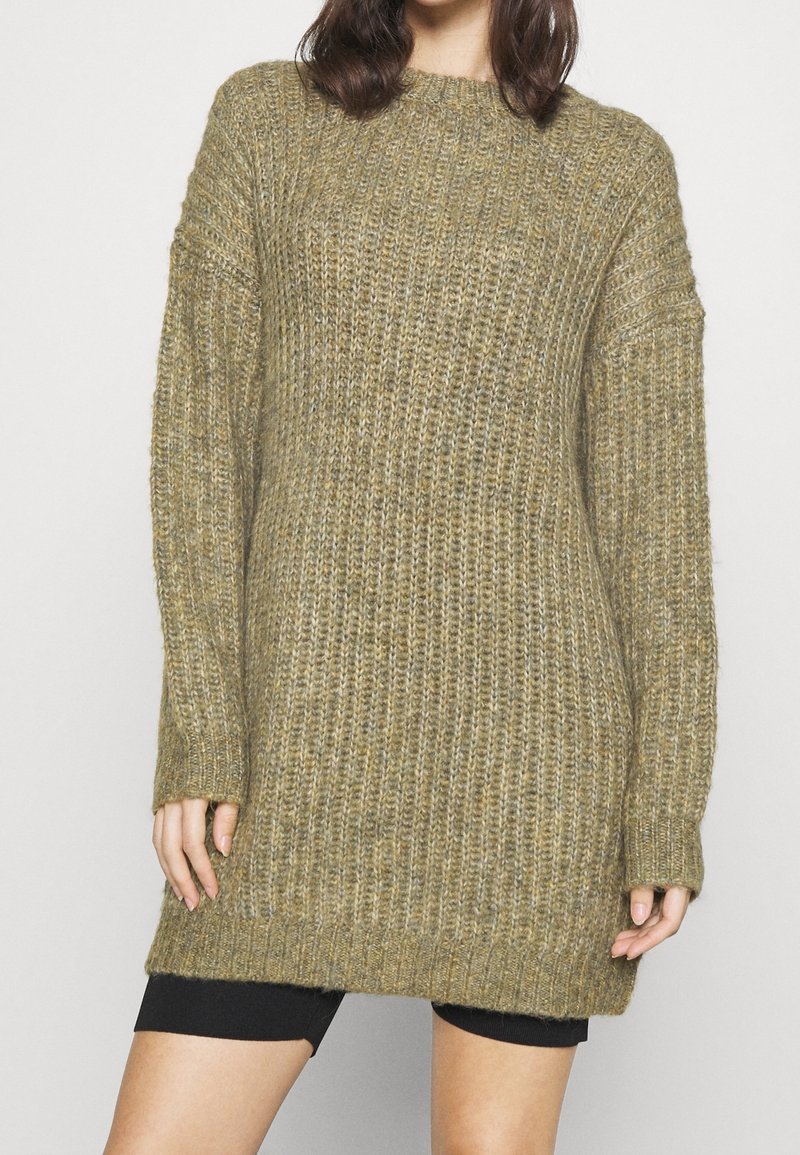 Gestrickter Pullover in Olivgrün, mit lockerer Passform, geripptem Texture, langen Ärmeln und rundem Halsausschnitt. Der Saum reicht bis über die Oberschenkel.