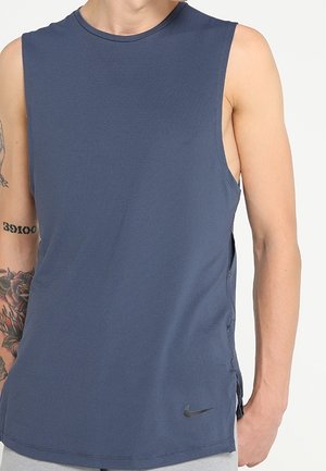 Granatowy sportowy podkoszulek bez rękawów noszony przez osobę z widocznymi tatuażami na ramionach oraz logo Nike przy brzegu.