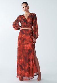 Abito lungo e fluente in sfumature di arancione e nero, caratterizzato da un design avvolgente, maniche a palloncino e uno spacco alto fino alla coscia.