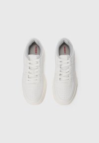 White sneakers with perforated texture and a smooth leather finish. Features laces, padded collar, and a small red logo on the tongue.