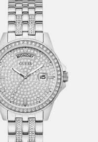 Srebrny zegarek ze stali nierdzewnej z twarzą wysadzaną kryształami, z wyświetlaczem daty i wskaźnikiem dnia na godzinie 12.