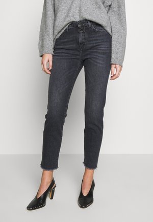 Personne portant un jean skinny taille haute gris foncé avec des ourlets effilochés, un pull en maille gris et des chaussures slingback à talons hauts noires cloutées.