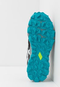Scarpa sportiva nera e grigia con suola in gomma testurizzata color turchese, caratterizzata da schemi di presa pronunciati e un dettaglio accentato giallo.