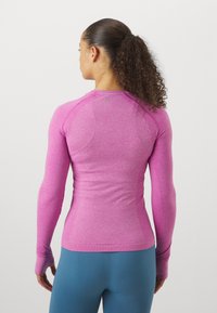 Dolga majica za vadbo v heather pink barvi, z neobičajno teksturo, raglan rokavi in otvorinami za palce na manšetah za dodatno zaščito.