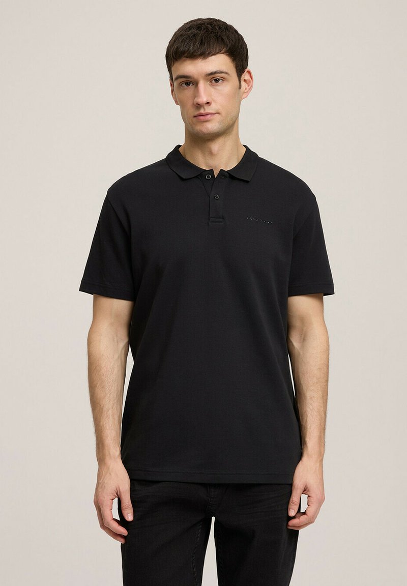Czarna koszulka polo z bawełny. Posiada kołnierzyk, zapięcie na trzy guziki oraz subtelne logo na piersi. Krótkie rękawy i standardowy krój.