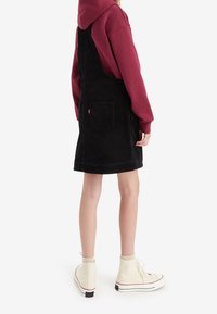 Černé kordové šaty s nastavovacími ramínky a zadní kapsou. Spárované s červenou mikinou a bílými vysokými teniskami.