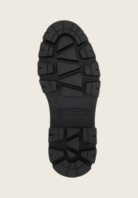 Suela de zapato de goma negra con superficie texturizada, que presenta profundas ranuras y patrones para una mejor tracción, marcada con la marca "TOM TAILOR".