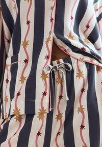 Baumwoll-Pyjama-Set mit navy- und weißen Streifen, pinken Wellenlinien sowie Sternmustern in Rot und Gold. Enthält ein Hemd mit Knopfleiste und eine Hose mit Kordelzug.