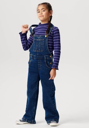 Donkerblauwe denim overall met een losse pasvorm, voorzien van verstelbare schouderbanden, voorzakken en een gestreepte paarse lange mouwen shirt eronder.