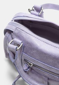Sac à main en daim lavande avec une fermeture éclair argentée partiellement ouverte, comportant une poche zippée à l'avant et une bandoulière ajustable avec des détails en métal.