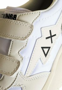Sneaker bianco con tomaia in pelle liscia e sovrapposizione in tessuto testurizzato. Accenti neri distintivi nel design e chiusura con cinturino in Velcro.