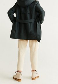 Czarny płaszcz z kapturem, związany w talii, w połączeniu z kremowymi spodniami typu cargo i beżowymi botkami sznurowanymi z grubą, brązową podeszwą.