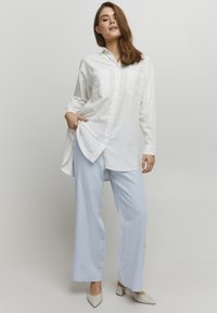 Witte langemouwen overhemd met twee borstzakken; gecombineerd met lichtblauwe wijde broek en beige blokhak schoenen.